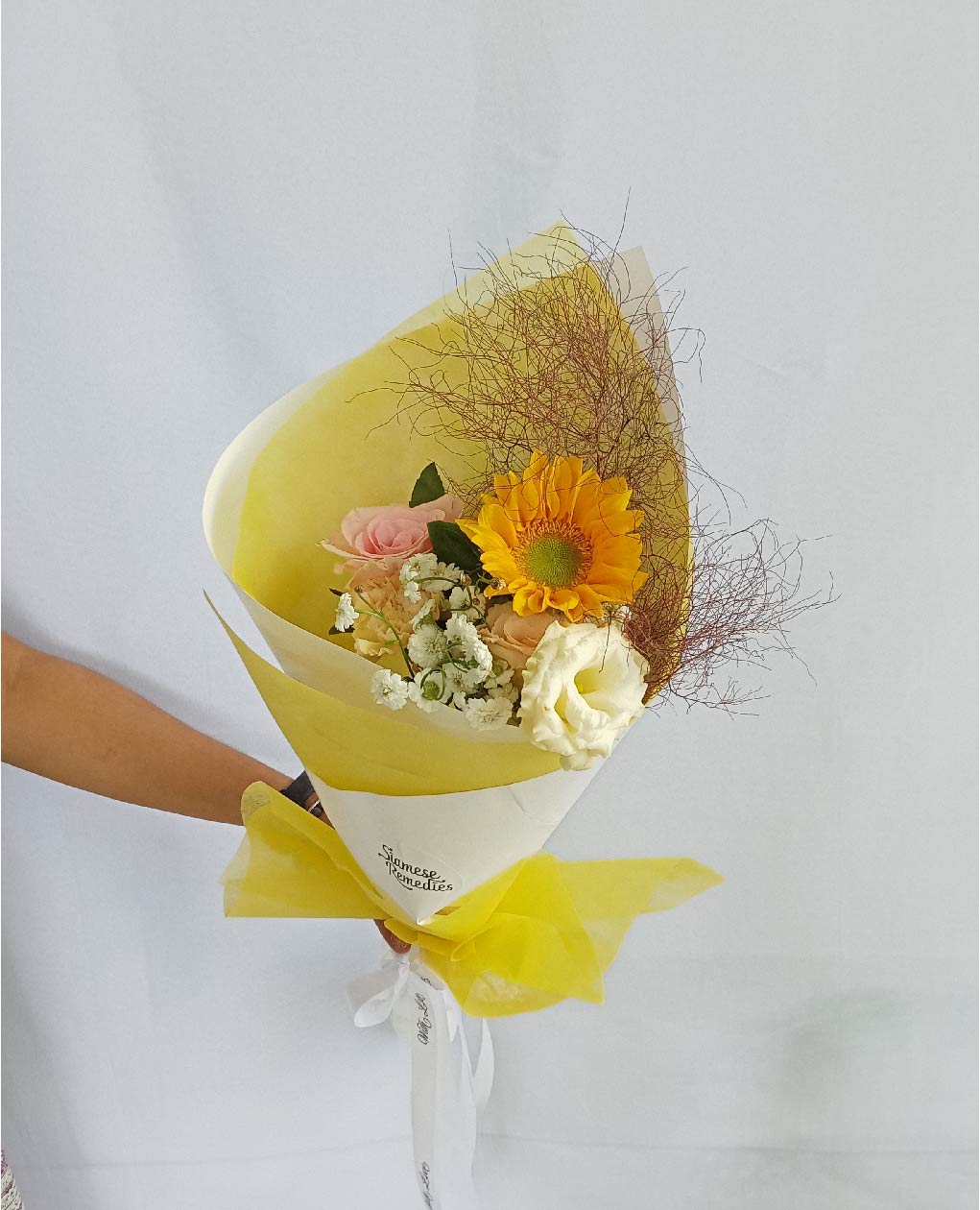 A Phuket flower bouquet featuring a vibrant sunflower, peach roses, cream lisianthuses, and baby's breath, perfect for brightening any occasion.