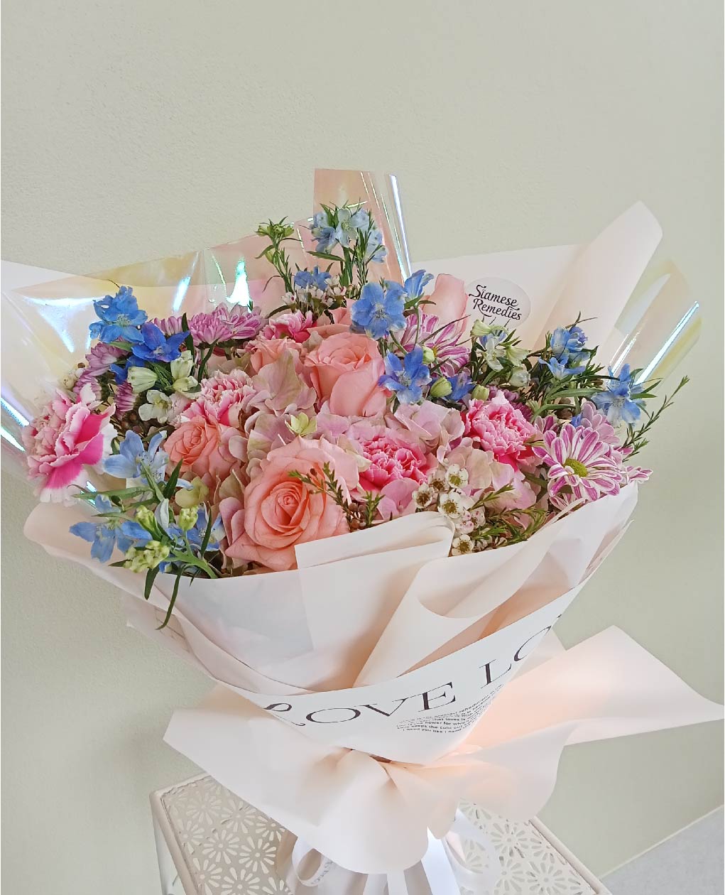 Soft Symphony bouquet with peach roses, pink carnations, blue delphiniums, and pastel flowers, perfect for special occasions in Phuket.