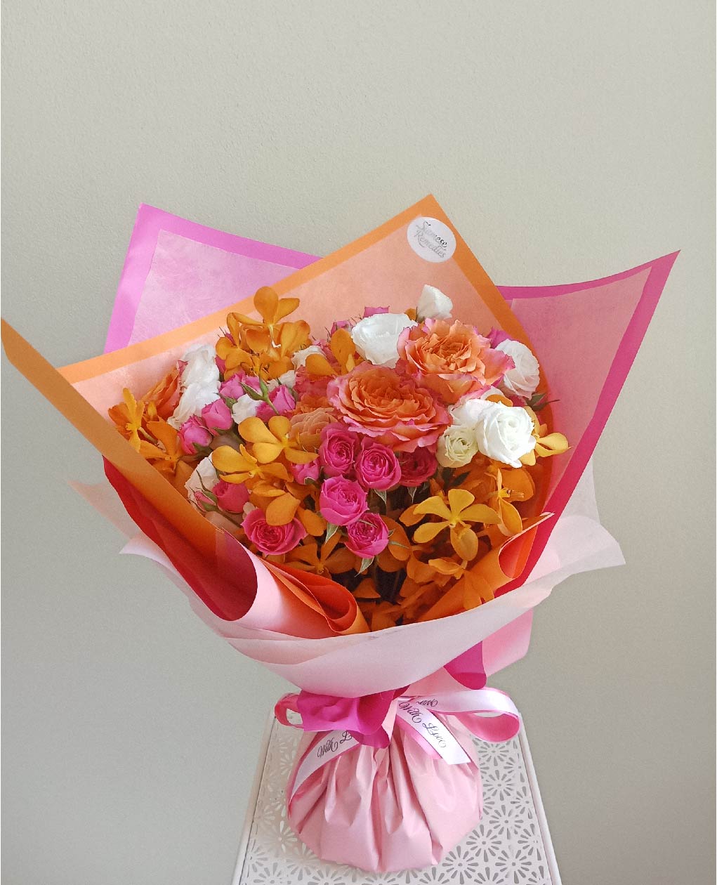 Phuket bouquet featuring vibrant orange and pink roses, white spray roses, and yellow orchids. Perfect for romantic occasions or celebrations.